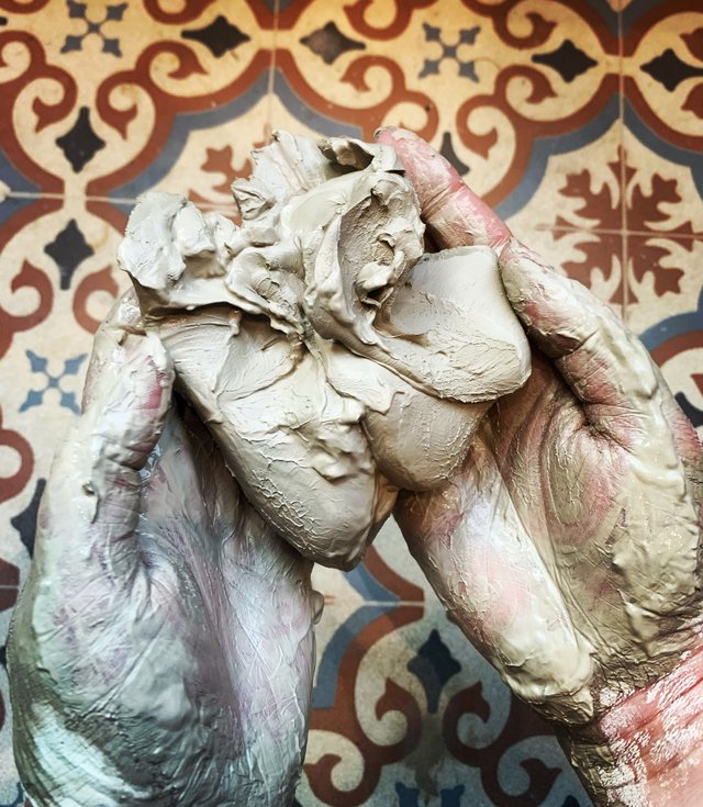 A person's upper body is covered in textured, greenish-pink paint. The background features a patterned tiled wall with blue, red, and cream colors.